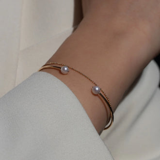 Bangle WAVE in Rose gold with two white pearls worn on wrist with filigree gold bracelet