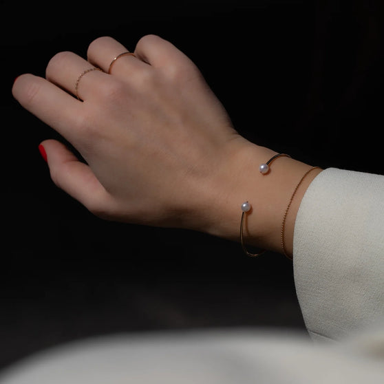 Hand of woman with gold rings and gold bangle wave with pearls and little gold bracelet