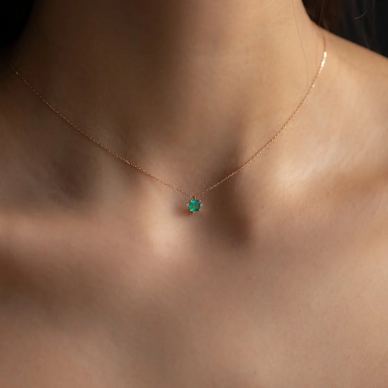 cleavage of woman wearing rose gold necklace with emerald and diamond pendant