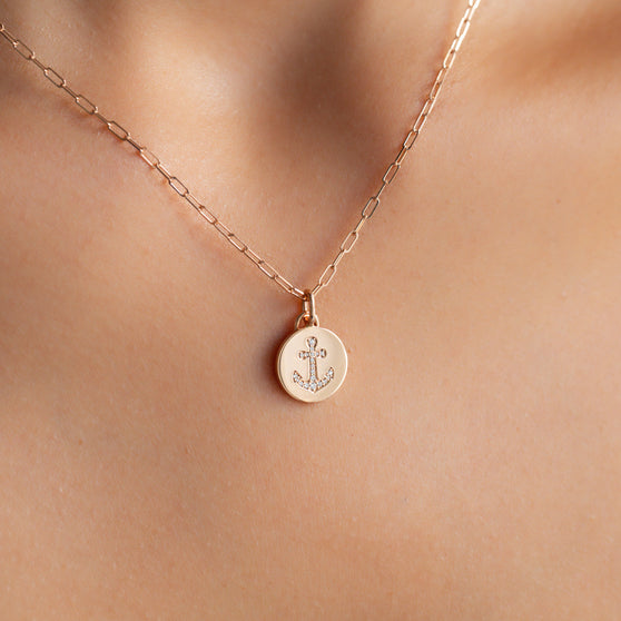 close up of cleavage with fine 18 KT rose gold link chain necklace and round pendant with anchor symbol and white diamonds