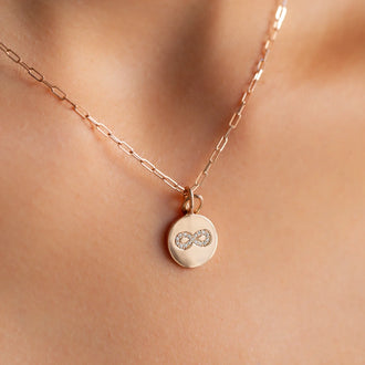 close up of cleavage with 18 kt rose gold link chain necklace with round coin pendant with eternity symbol in white diamonds