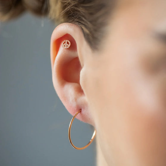 blond woman wearing a stunning 18 KT rose gold ear stud piercing in the shape of a peace-sign adorned with brilliant white diamonds