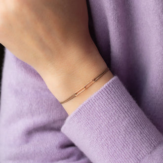 Wristband with beige ribbon and chain links in 18 KT rose gold worn on wrist of person in lilac sweater