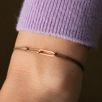 closeup of Wristband with beige ribbon and chain links in 18 KT rose gold worn on wrist of person in lilac sweater