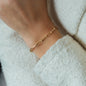 detail of woman wearing white jacket and yellow gold chain bracelet