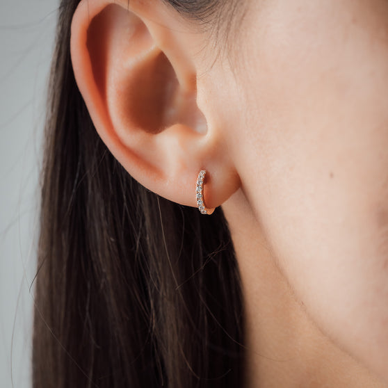 close up of ear from woman with dark hair and small earring in rose gold and with white diamonds