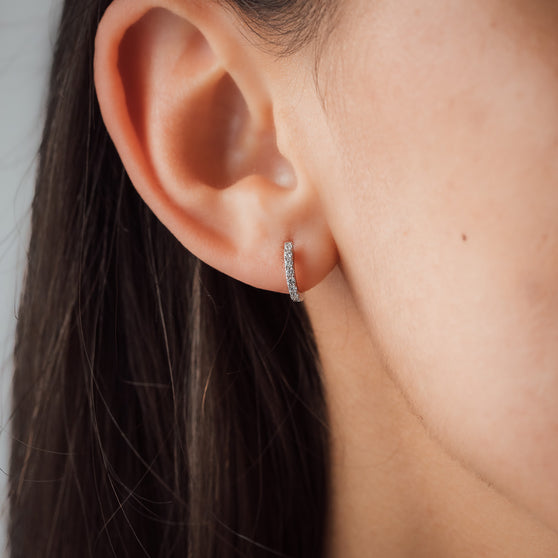 detail shot of woman's ear with small round diamond earring in white gold