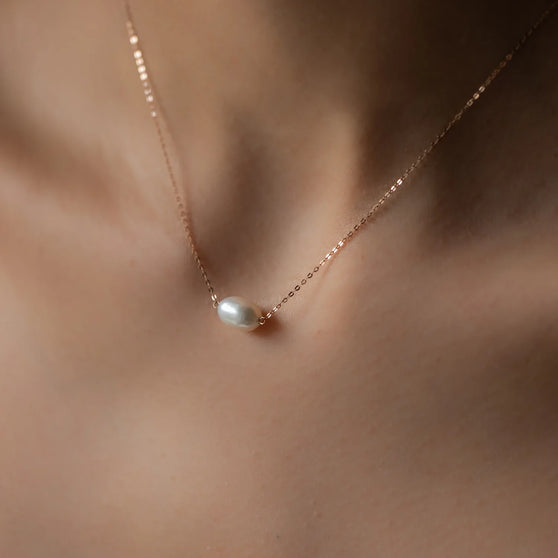 close up of womans cleavage wearing necklace hana with rose gold chain and big oval pearl pendant