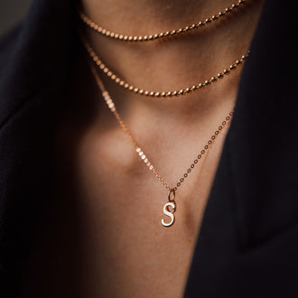 detail of neck with rosegold necklaces and letter s