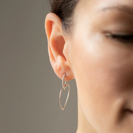 Woman wearing hoop earring with white diamonds and pendant emotion in heart shape in silver