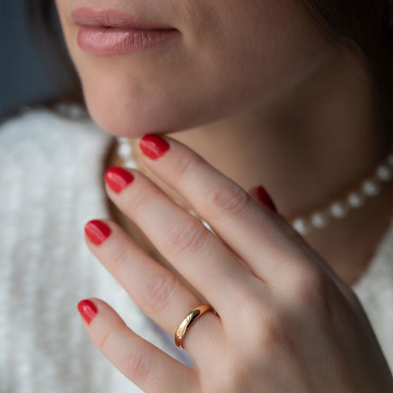 womans wearing white jacket, pearl necklace and rose gold wedding ring with hand on chin
