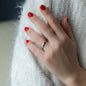 hand of woman in front of white background with red nail polish and white gold wedding ring