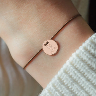 closeup of wrist of woman with wristband with rose gold pendant with rabbit symbol engraved