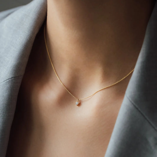 close up of woman’s cleavage wearing a grey blazer with necklace SOUL with a white diamond in yellow gold